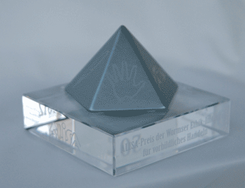 Ein animiertes GIF, das die blaumetallic-farbene 5seitige Pyramide auf dem Sockel aus transparentem Plexiglas zeigt. Dieses Preisobjekt dreht sich um die senkrechte Achse.